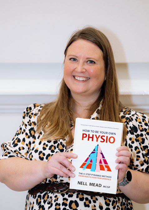 A smiling woman holds a book while facing the camera.