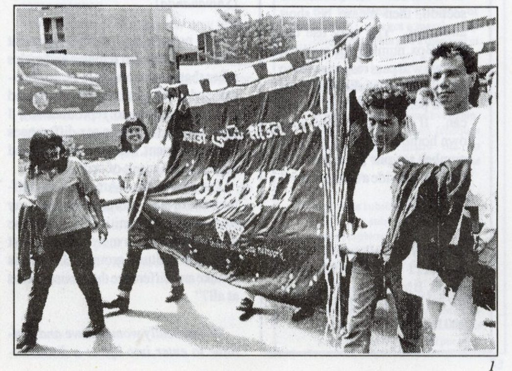 Black and white photo of people marching, holding a large Shakti banner