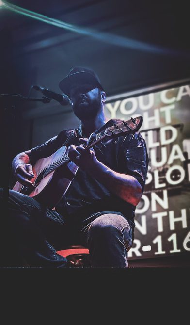 A close-up shot, from underneath, of a singer/guitarist on stage in the Great Hall.