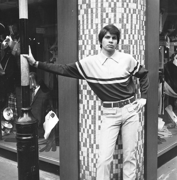 A Black and white photo of a male model posing outside a clothing shop on Carnaby Street in the 1960s
