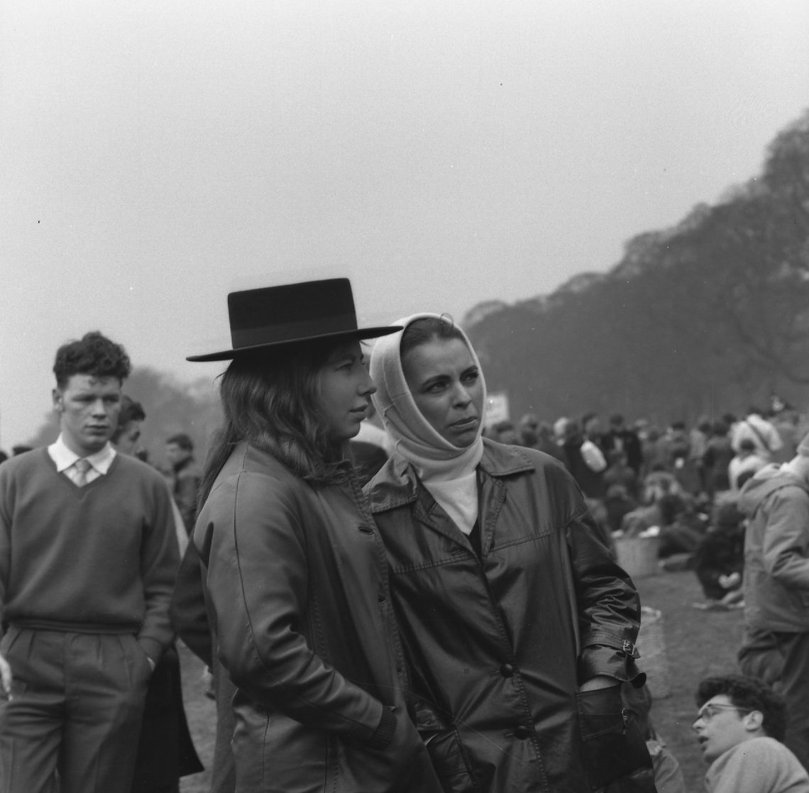 A black and white photo of protesters at the Aldermaston March. Two women are the focus of the photo. One wears a brimmed hat, the other a headscarf