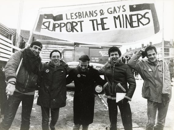 Members of Lesbians & Gays Support The Miners, stood outside in winter with a large banner protesting